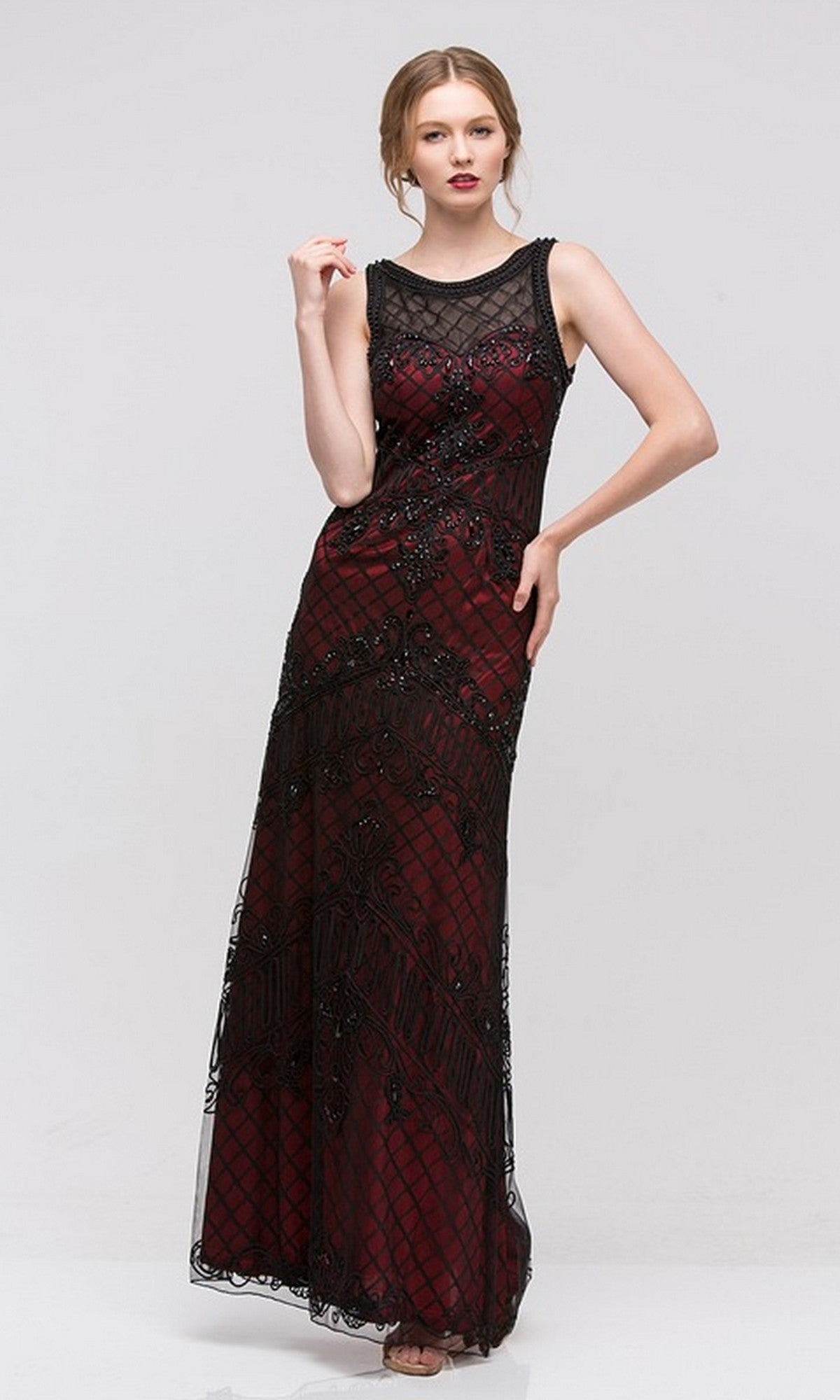 A woman models the Eureka 3915 Long Formal Dress, featuring a sleeveless design, illusion neckline, decorative beading, and a sheer black floor-length overlay, standing against a plain light background.